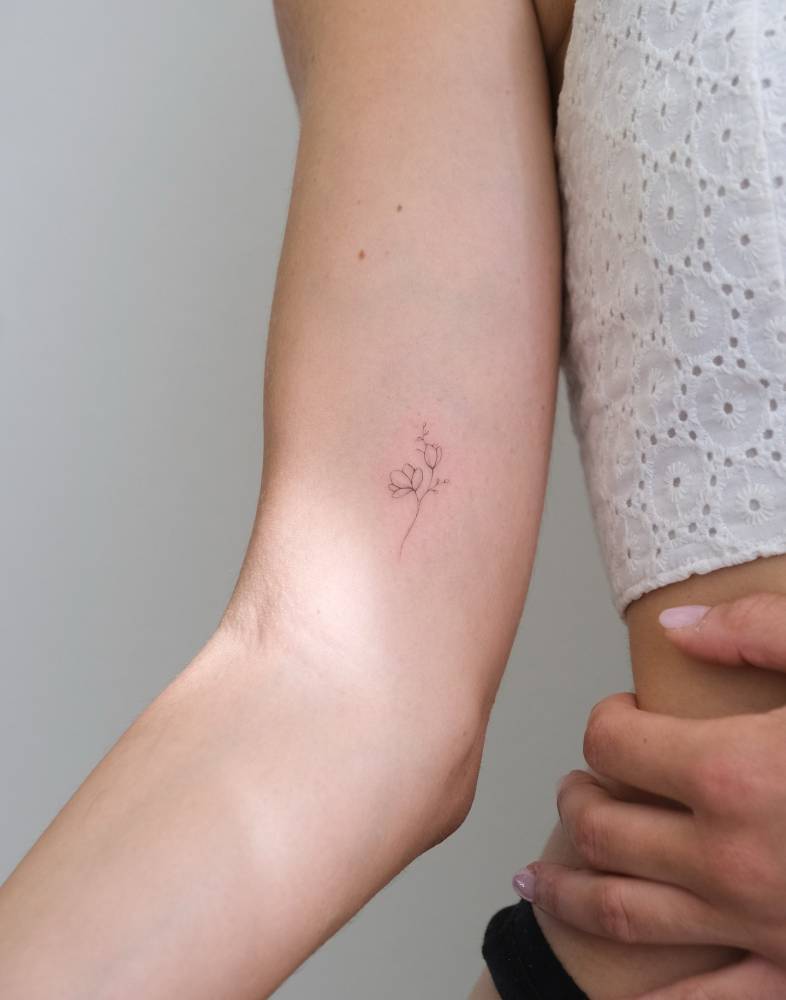 Little flowers tattoo in fine line style located on the inner arm.