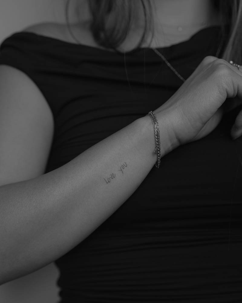"Love you" lettering tattoo in handwritten font located on the wrist.