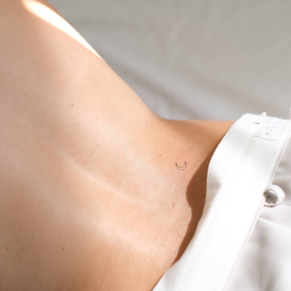Tiny minimalistic crescent moon tattoo placed on the lower back.