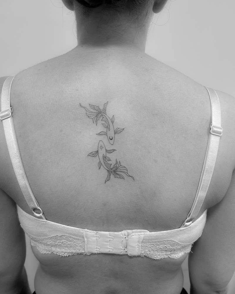 Tow opposite fish tattoo in fine line style done on the upper back.
