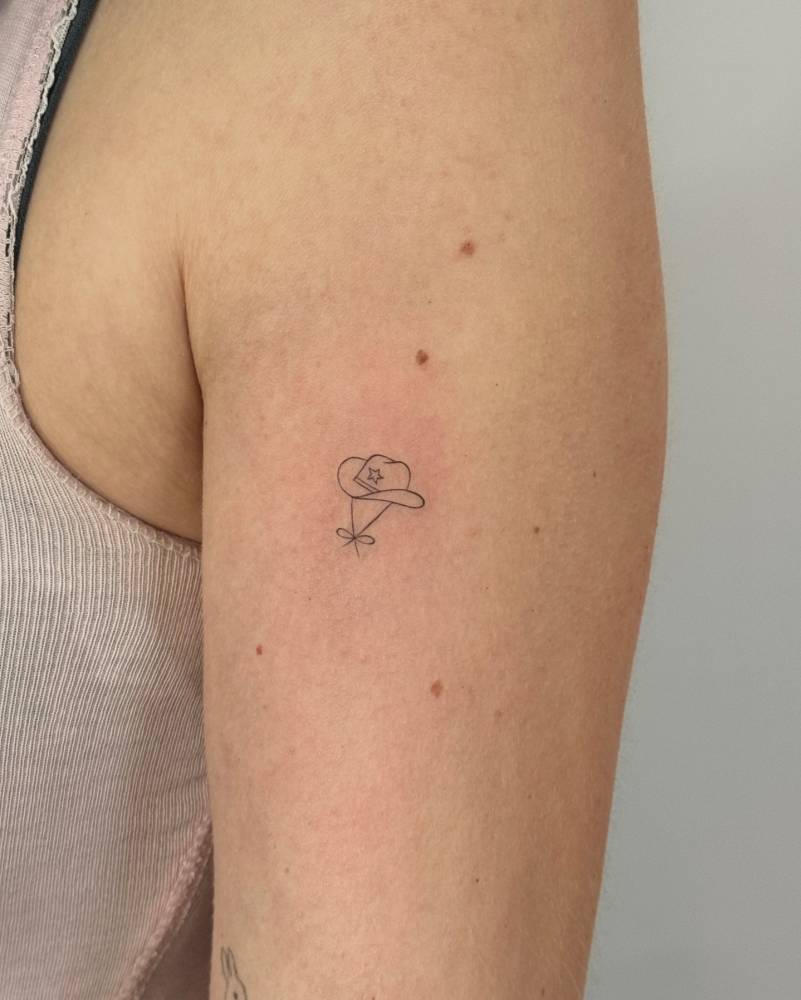 Fine line style cowboy hat tattoo located on the upper arm.