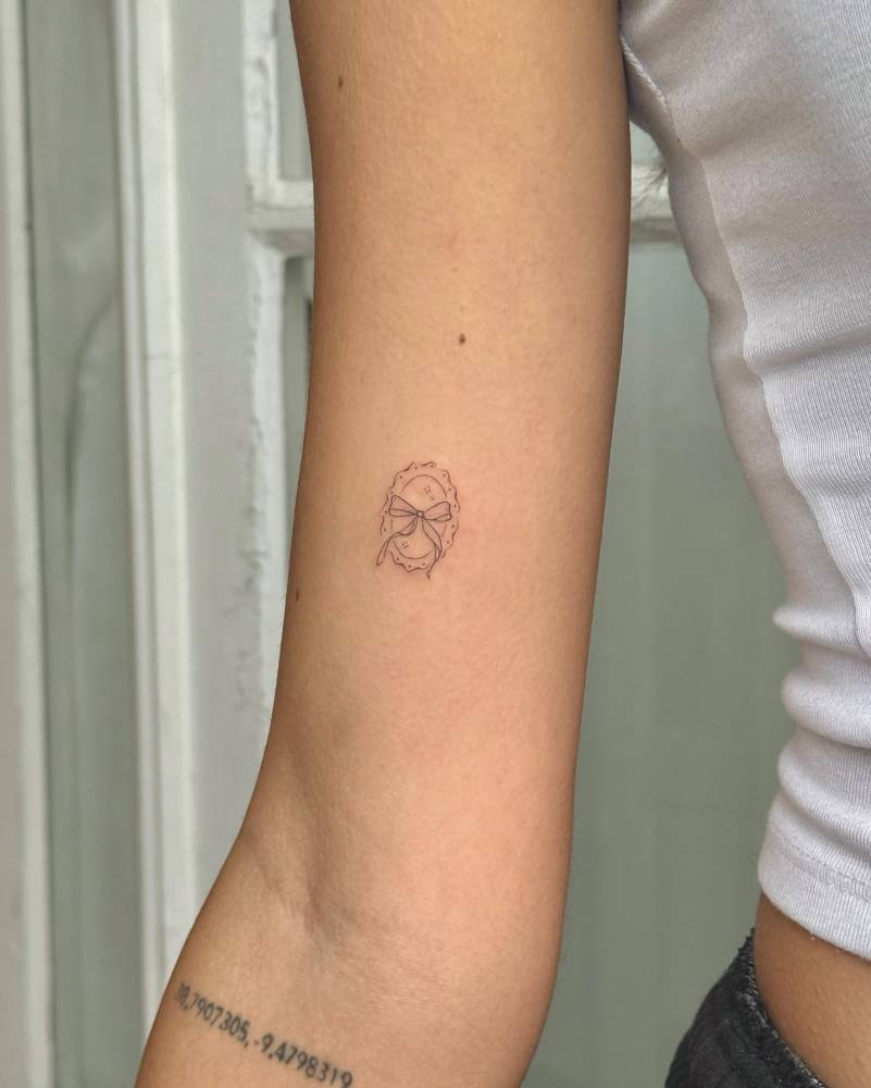 Bow tattoo located on the inner arm, done in fine line style.