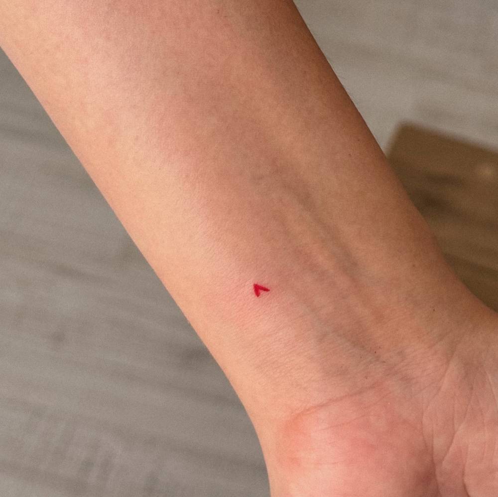 Micro red heart tattoo in minimalistic style done on the wrist.