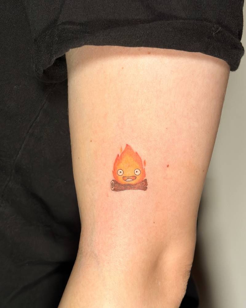 Cartoon style Calcifer tattoo located on the upper arm.