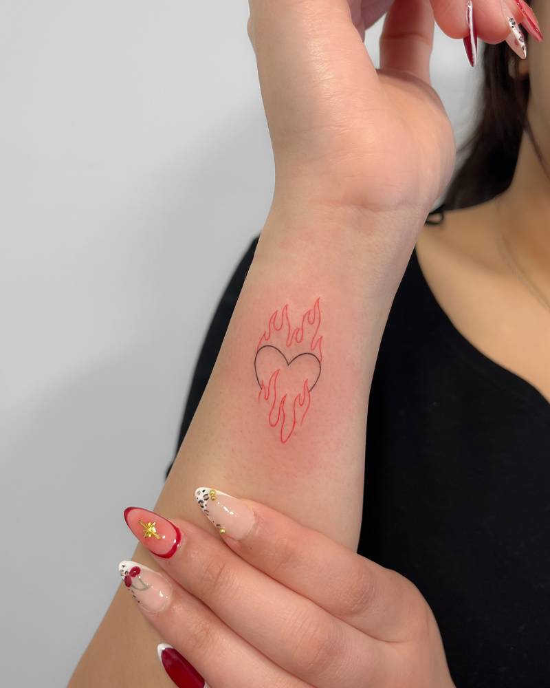 Flaming heart tattoo in fine line style located on the wrist.