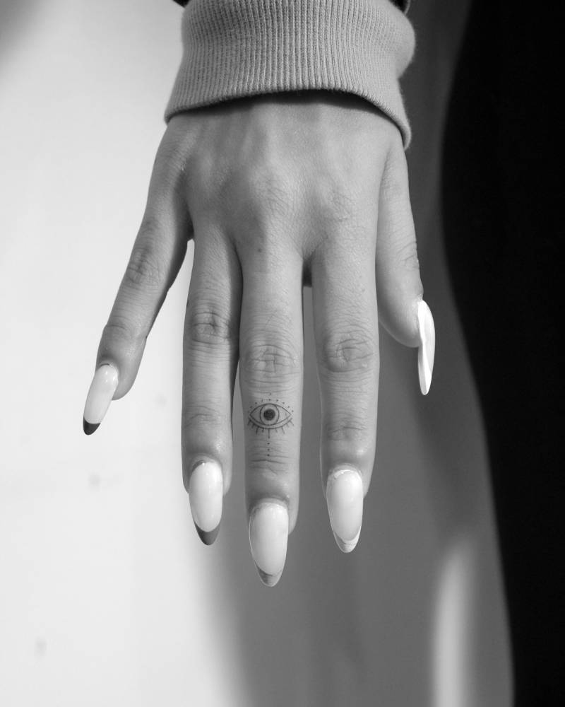Tiny evil eye tattoo in minimalistic style done on the finger.