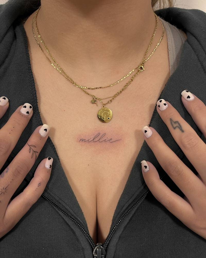 Handwritten lettering tattoo of the name "Millie" located on the chest.
