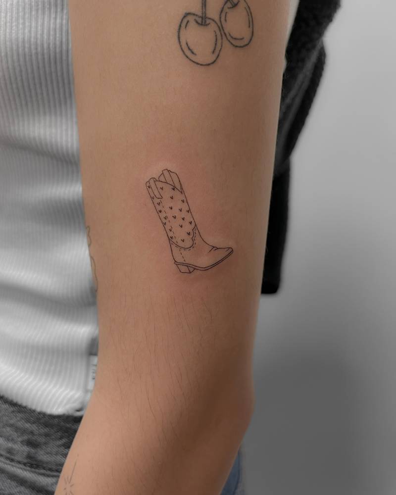 Fine line style cowboy boot tattoo located on the upper arm.
