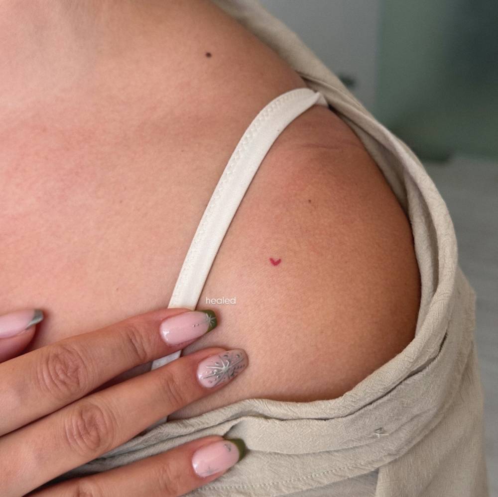 Tiny micro red heart tattoo located on the shoulder (healed).