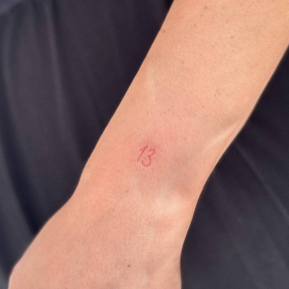 Lucky number "13" tattoo in red ink located on the wrist.