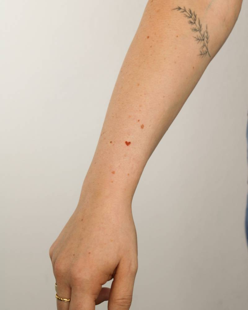 Little red heart tattoo located on the wrist, minimalistic style.