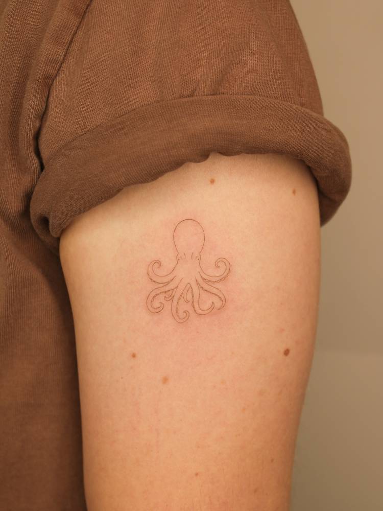Little tattoo of an octopus in fine line style placed on the upper arm.