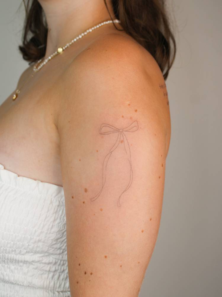 Fine line style bow tattooed on the upper arm.