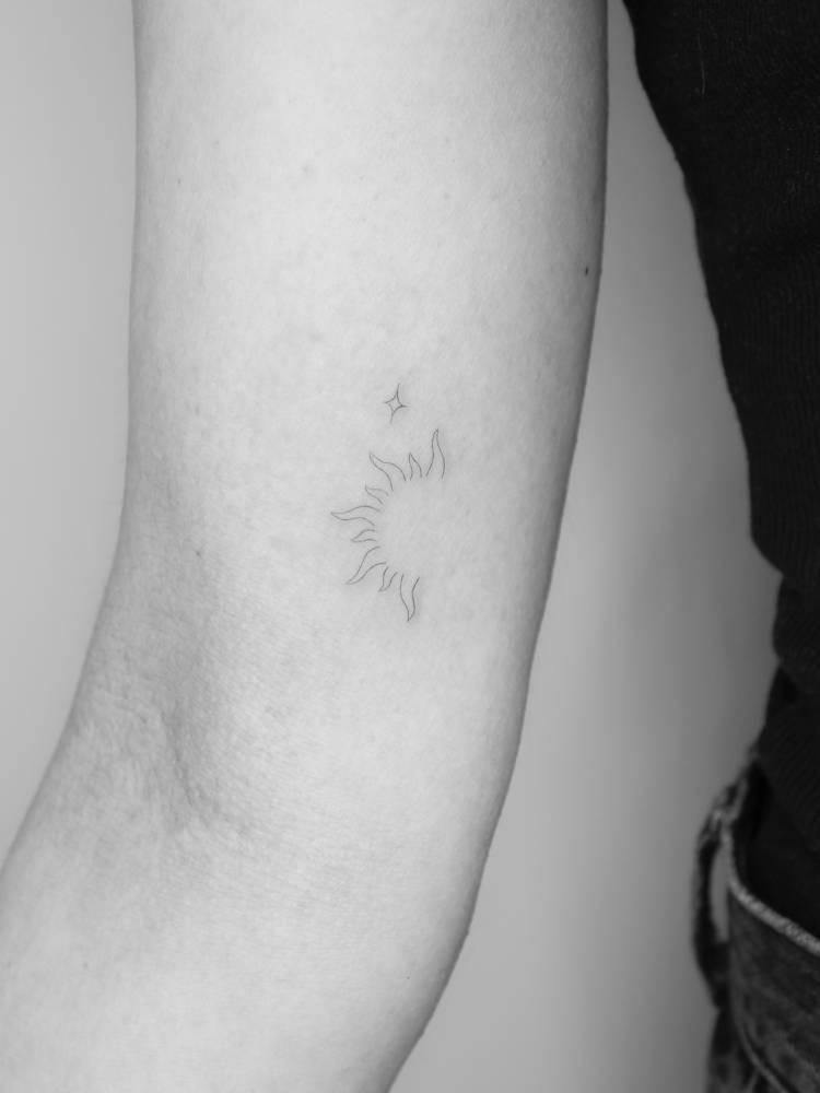 Fine line style sun tattoo located on the inner arm.