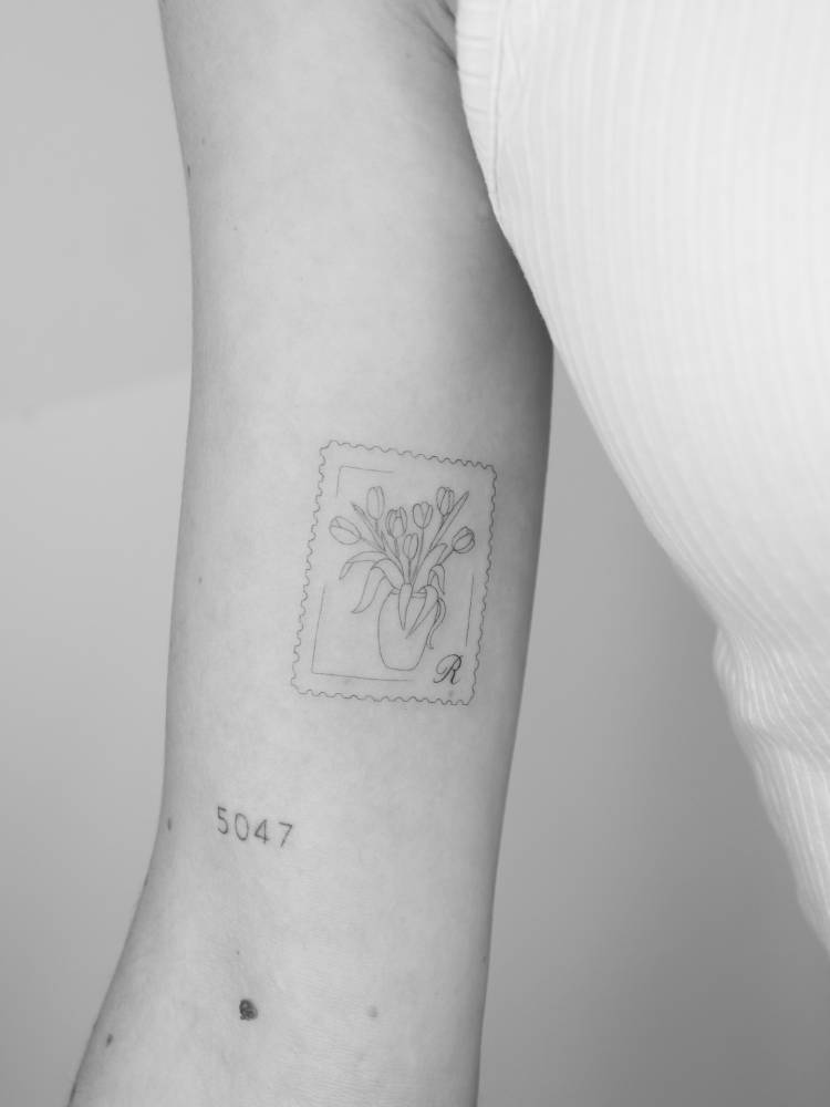 Tulip stamp tattoo placed on the inner arm, done in fine line style.