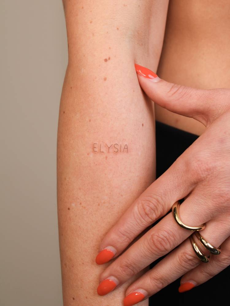 "Elysia" lettering tattoo located on the forearm.