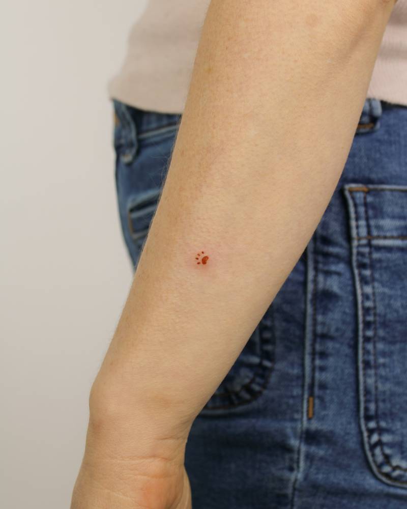 Micro dog paw print tattoo in red ink done on the forearm.
