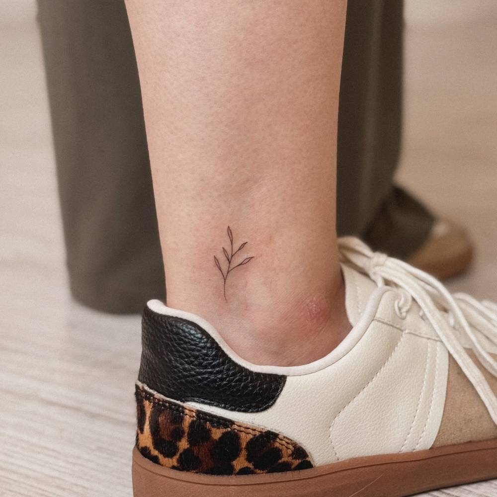 Minimalistic sprig tattoo in fine line style located on the ankle.