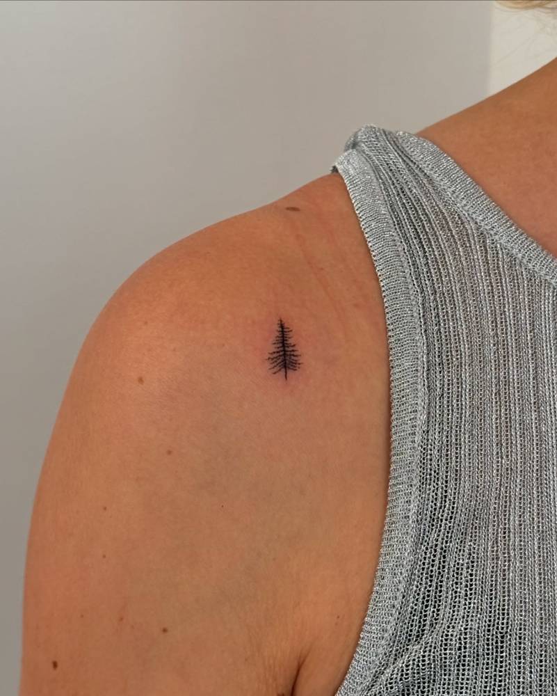 Pine tree tattoo in minimalistic style located on the shoulder.
