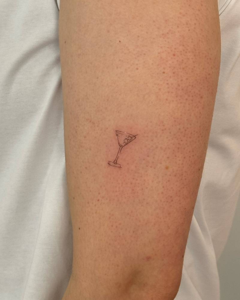 Martini cocktail tattoo in fine line style located on the upper arm.