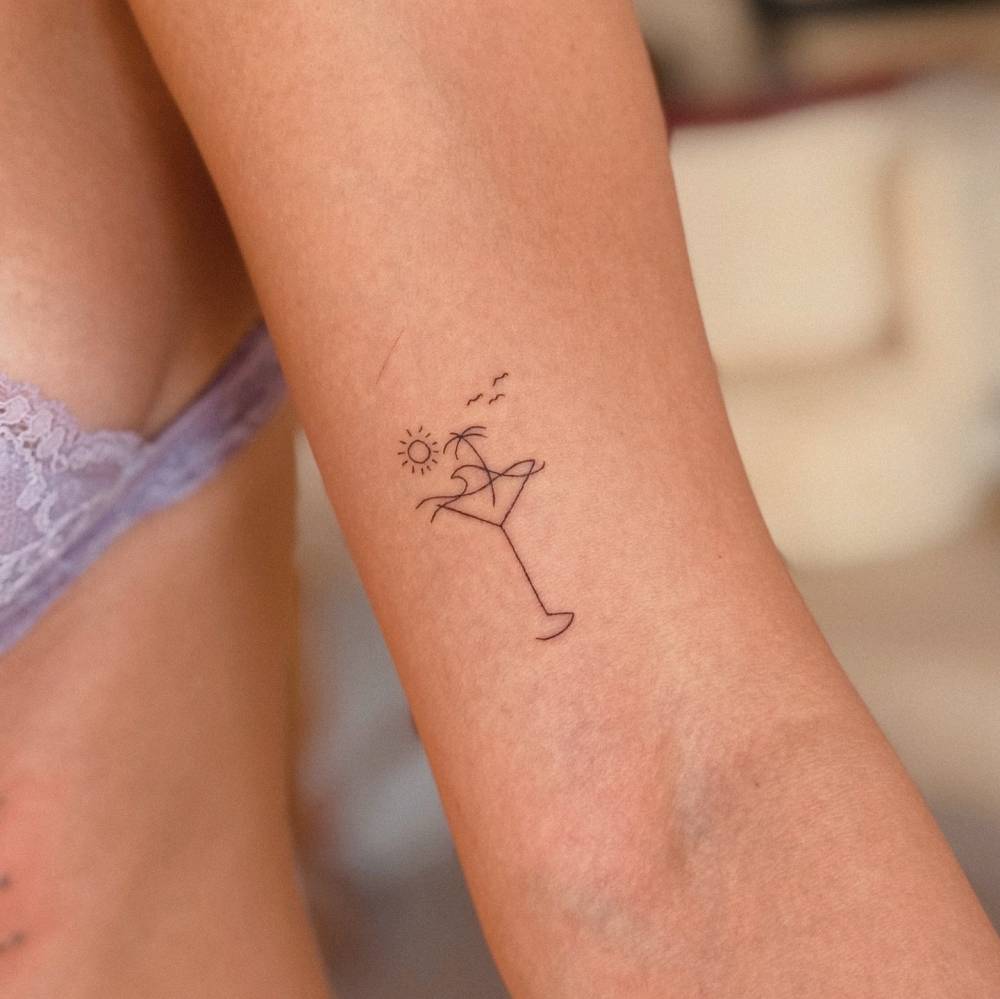 beach cocktail tattooed on the bicep, done in fine line style.