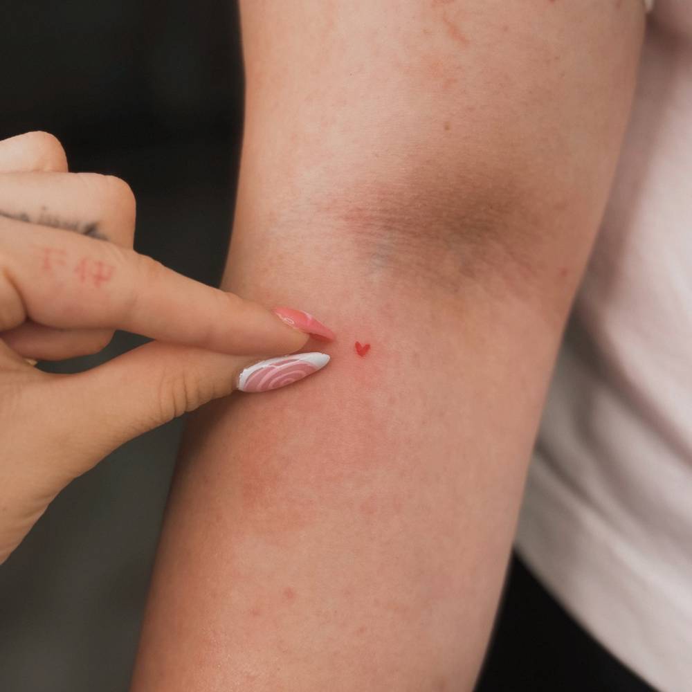 Super tiny red heart tattoo located on the elbow, minimalistic style.