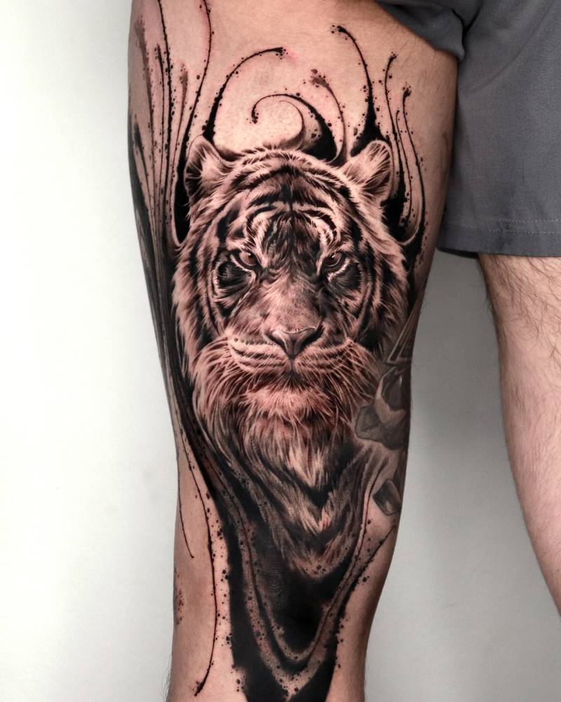 Tiger portrait tattoo in black an grey style located on the thigh.