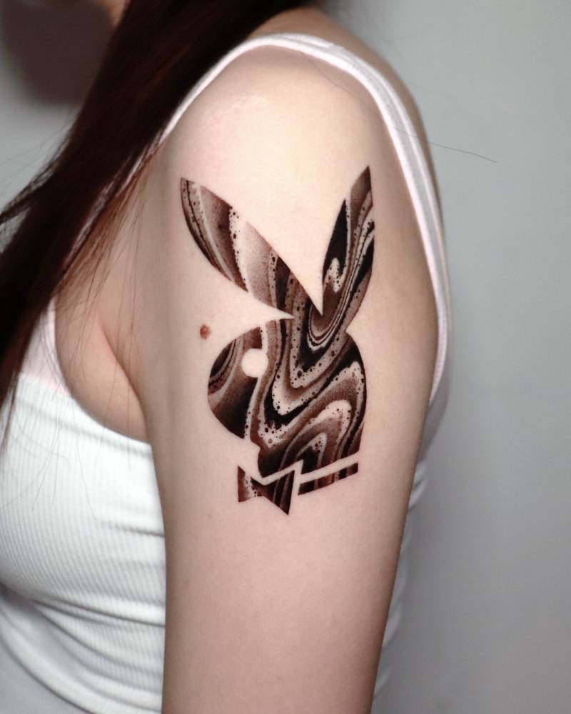 Playboy logo tattoo located on the upper arm, done in blackwork style.