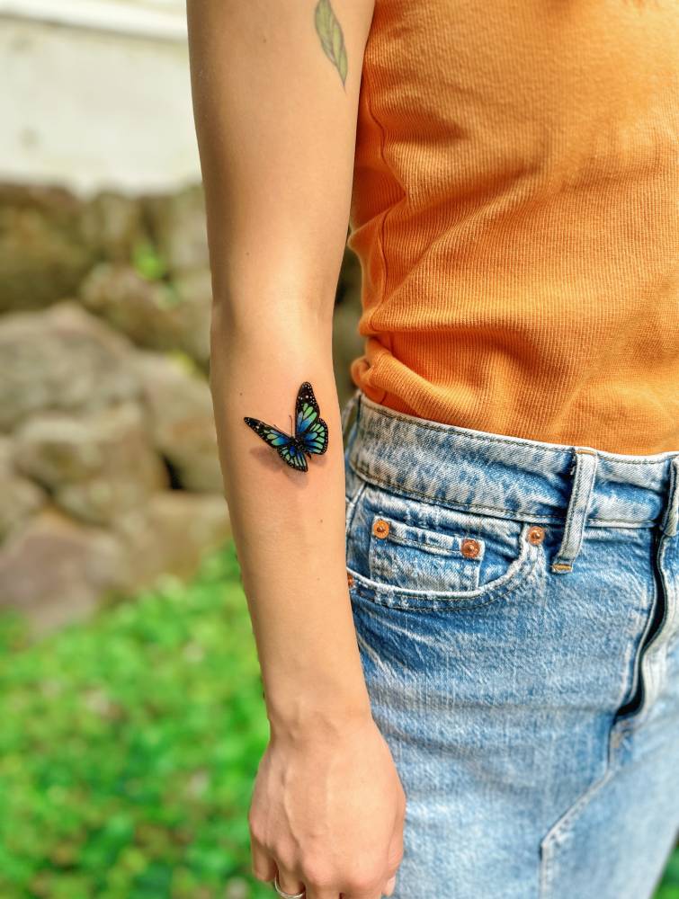 Micro-realistic style blue butterfly tattoo located on the forearm.
