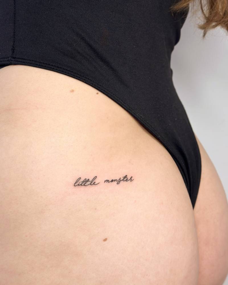 "Little monster" lettering tattoo in handwritten font located on the butt cheek.