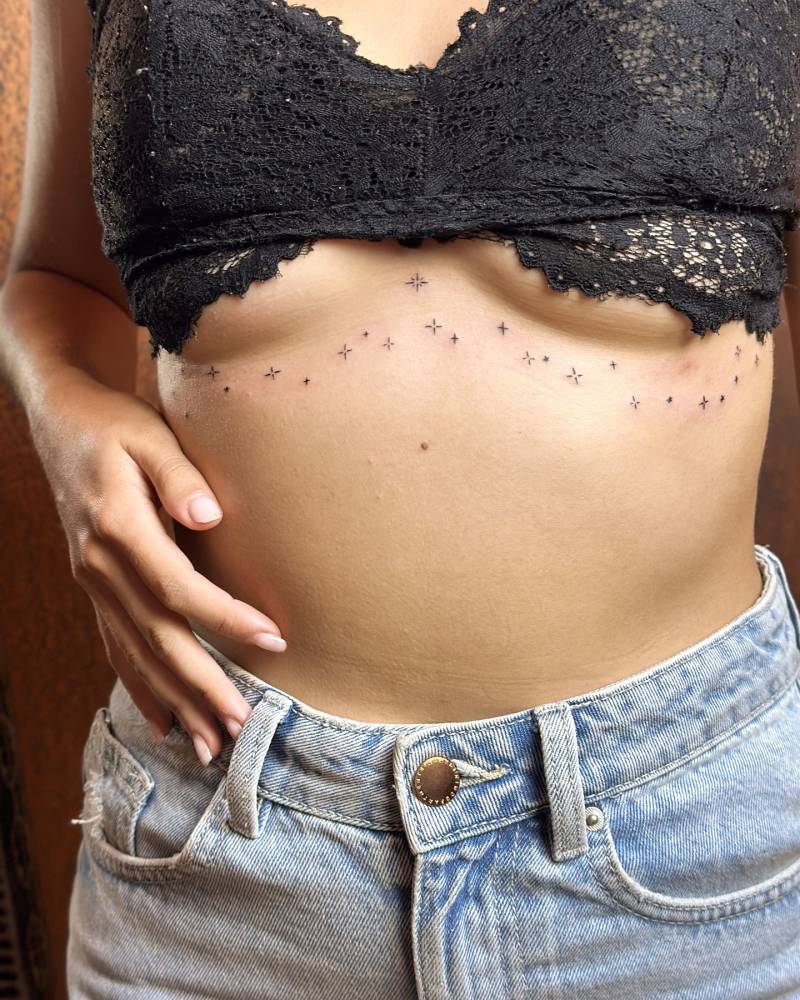 Sparkling stars tattoo placed on the under boob, done in minimalistic style.