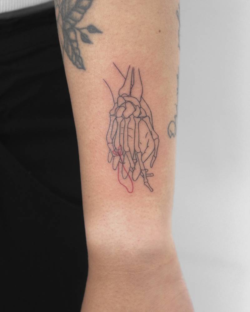 Holding hands tattoo located on the wrist, done in fine line style.