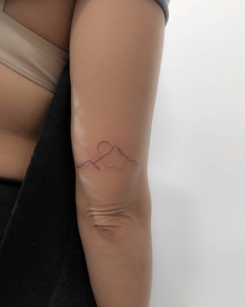 Continuous line mountain sunset tattoo located on the tricep.