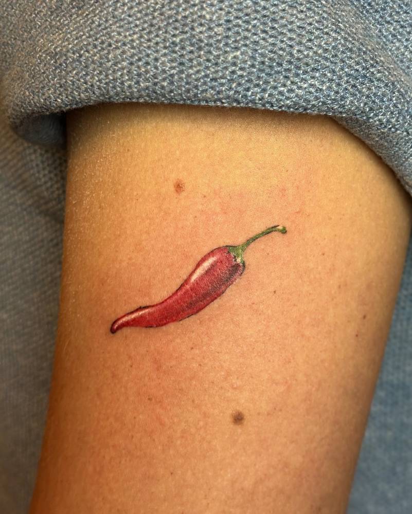Illustrative style red chili tattoo located on the upper arm.