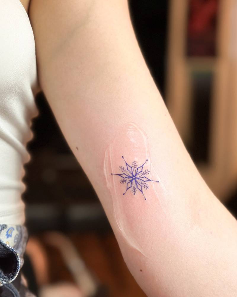 Snowflake tattoo in blue ink located on the inner arm.