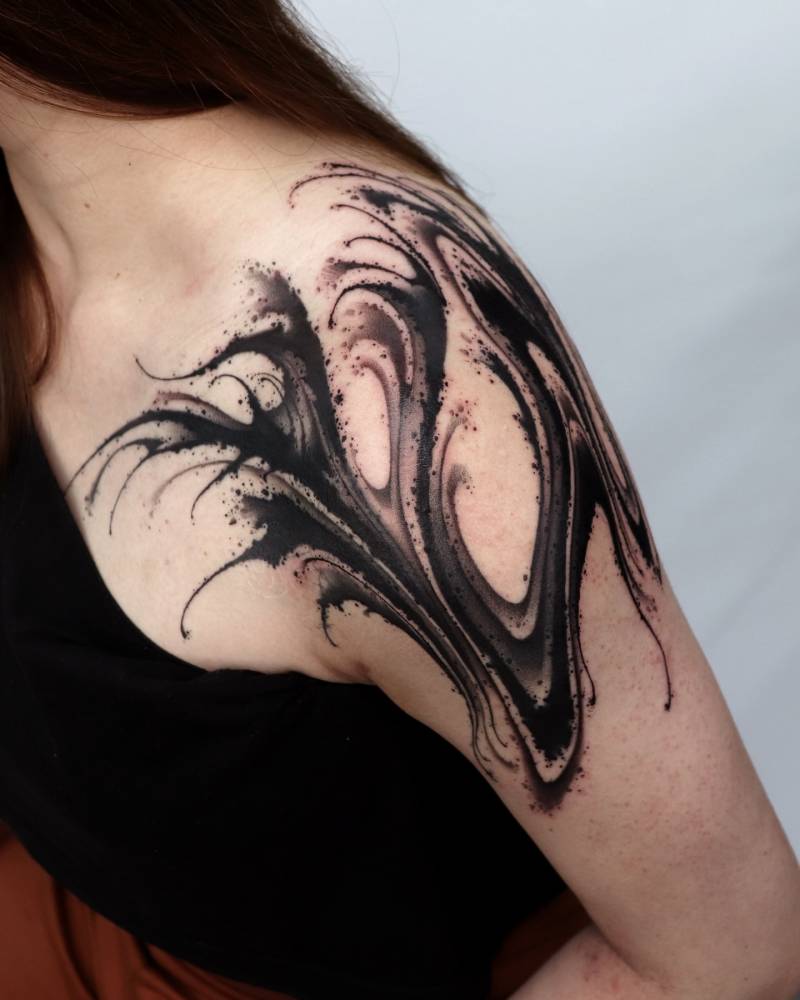 Abstract wave tattoo in blackwork style located on the shoulder.