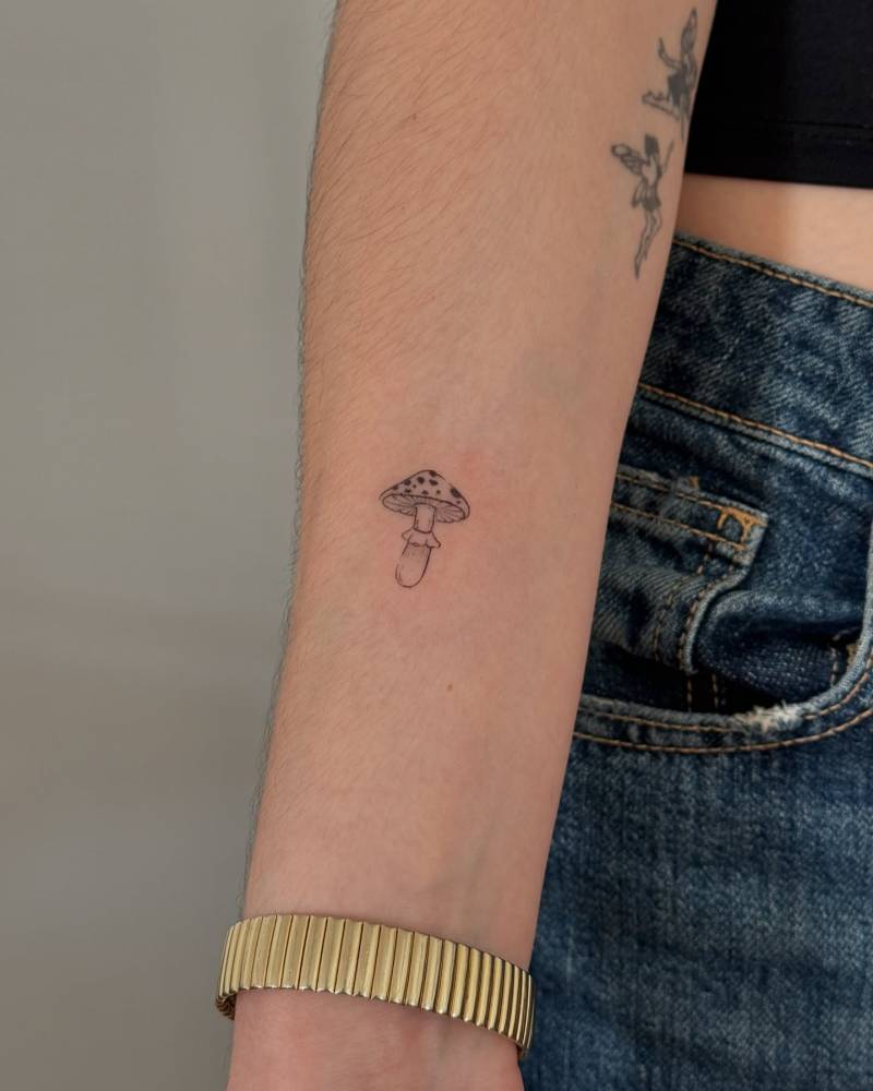 Little mushroom tattoo in illustrative style located on the inner forearm.