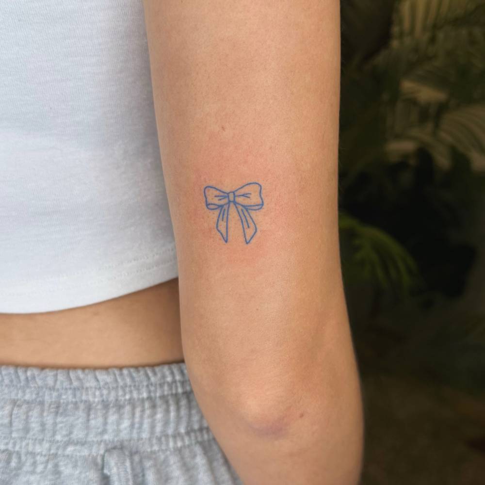 Hand poked blue bow tattoo done on the tricep, minimalistic style.