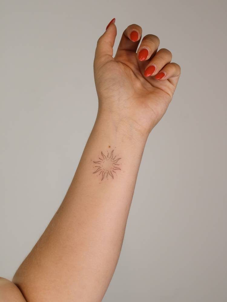 Little sun tattoo done in fine line style, located on the wrist.
