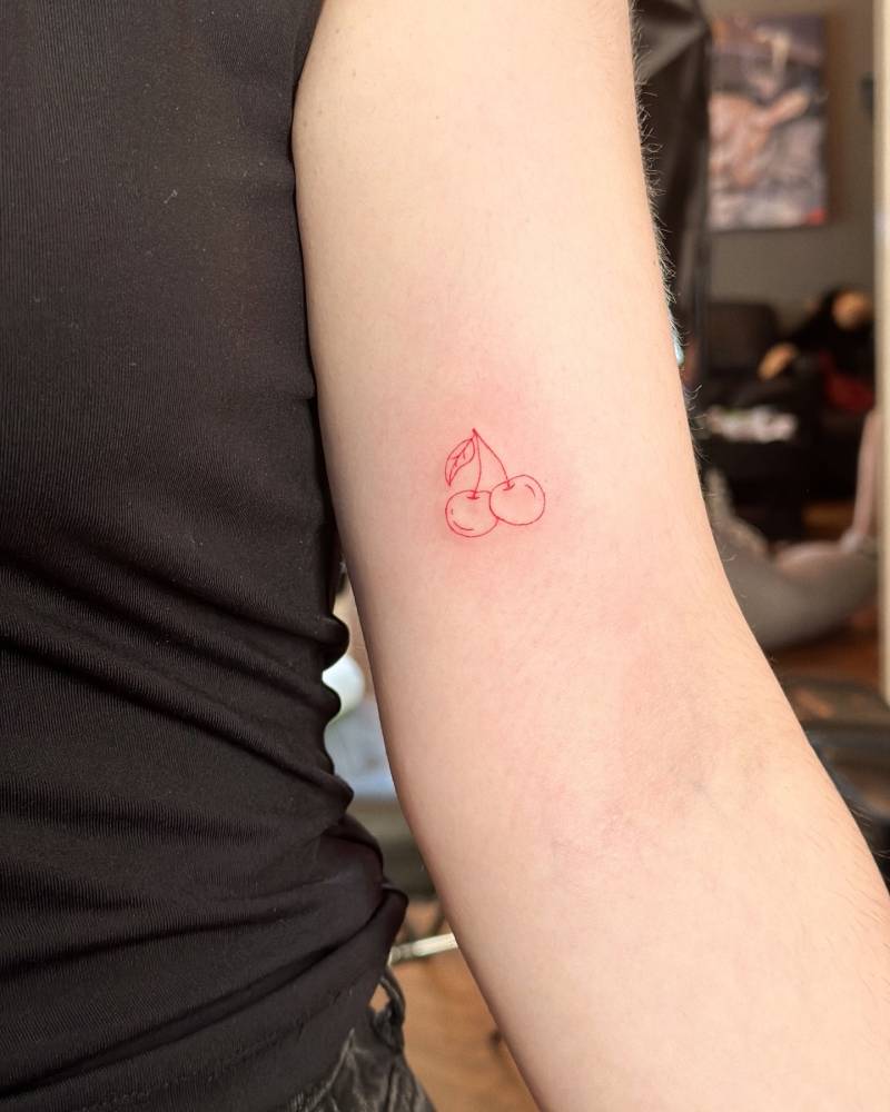 Fine line style red cherries tattoo located on the inner arm.
