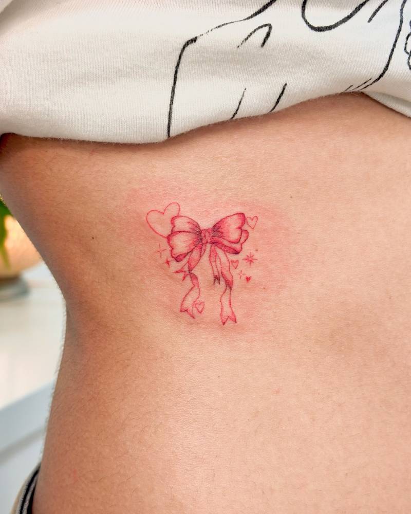 Red bow tattoo in illustrative style located on the rib.