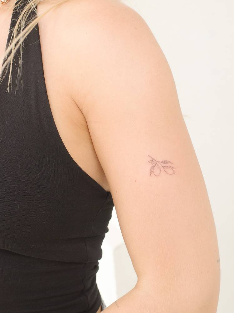 Little lemons tattooed on the upper arm, done in fine line style.