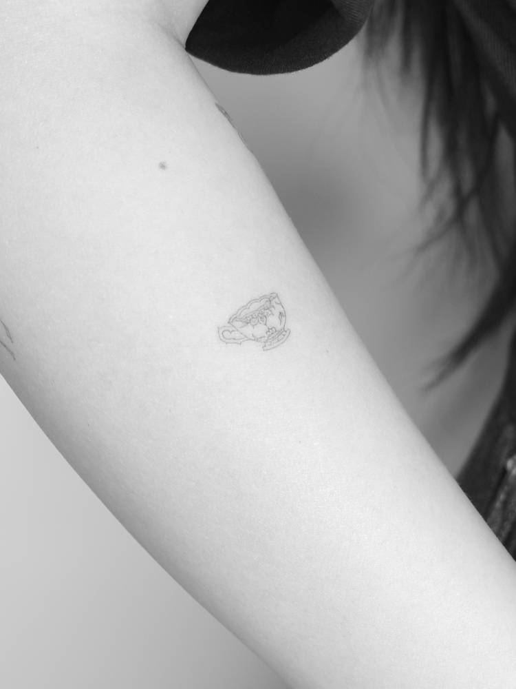 Teacup tattoo placed on the upper arm, done in fine line style.