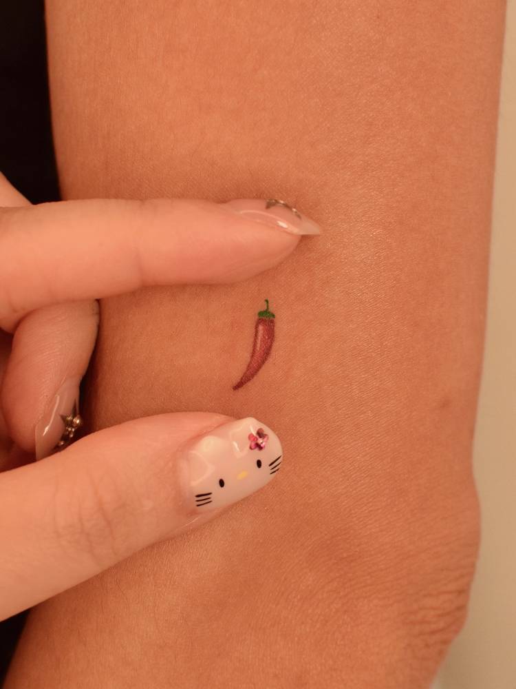 Tiny red chili pepper tattoo located on the upper arm, illustrative style.