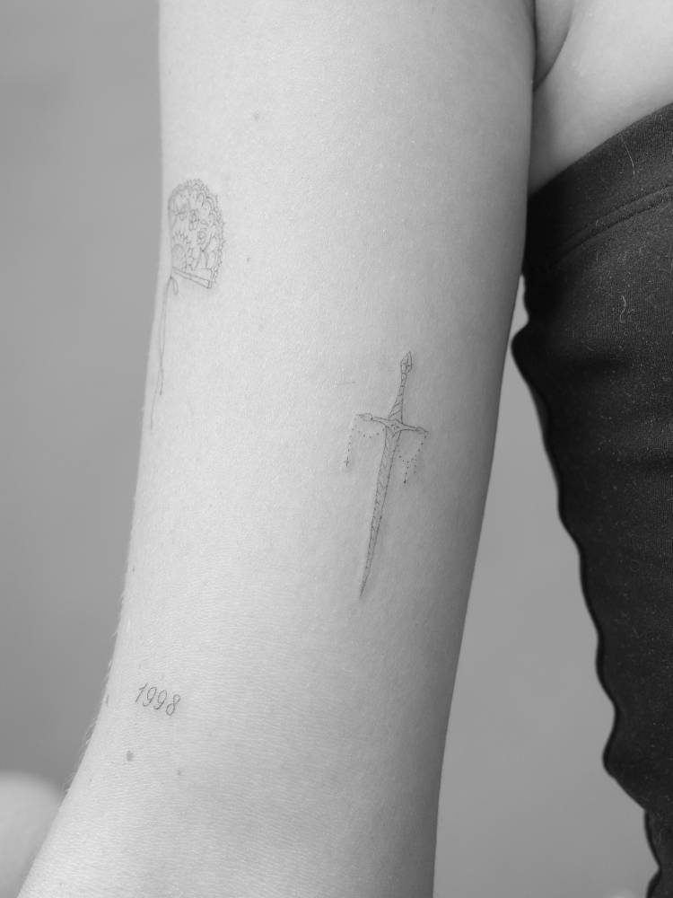 Tiny sword tattoo in fine line style placed on the inner arm.
