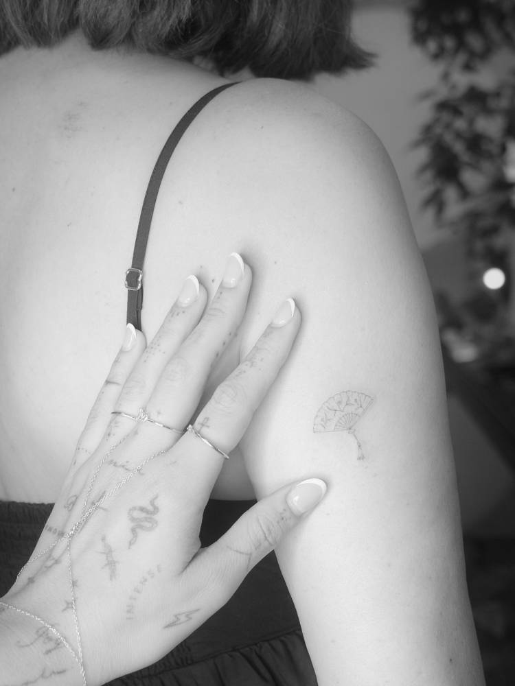 Hand fan tattoo in fine line style located on the upper arm.