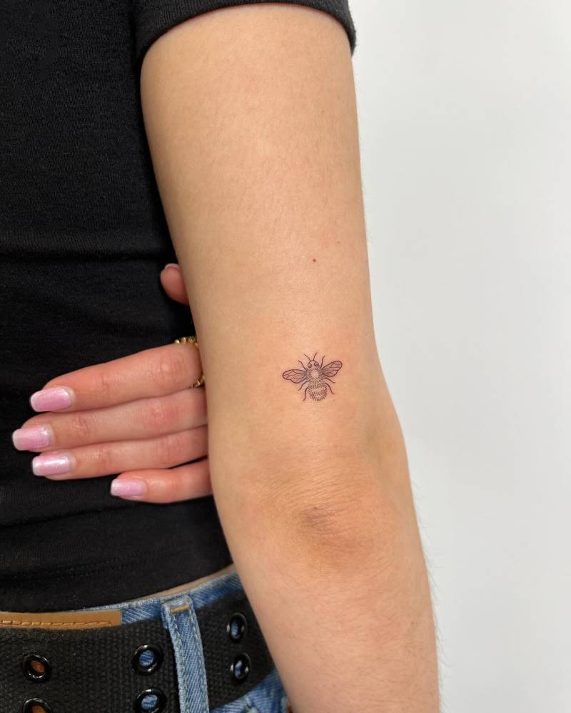 Tiny fine line style bee tattoo located on the tricep.