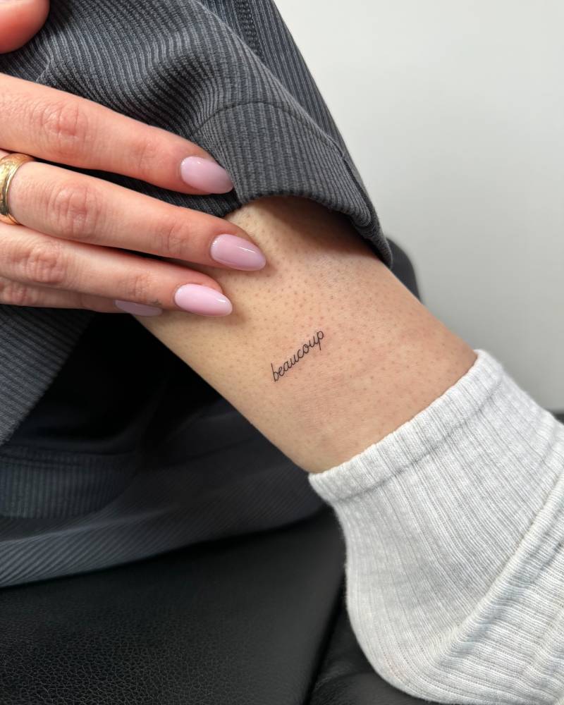 "Beaucoup" handwritten lettering tattoo located on the ankle.