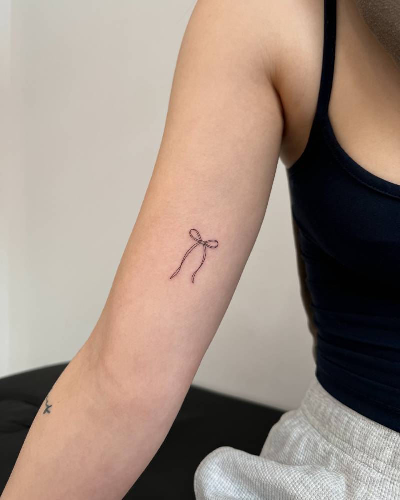 Bow tattoo placed on the inner arm, done in fine line style.