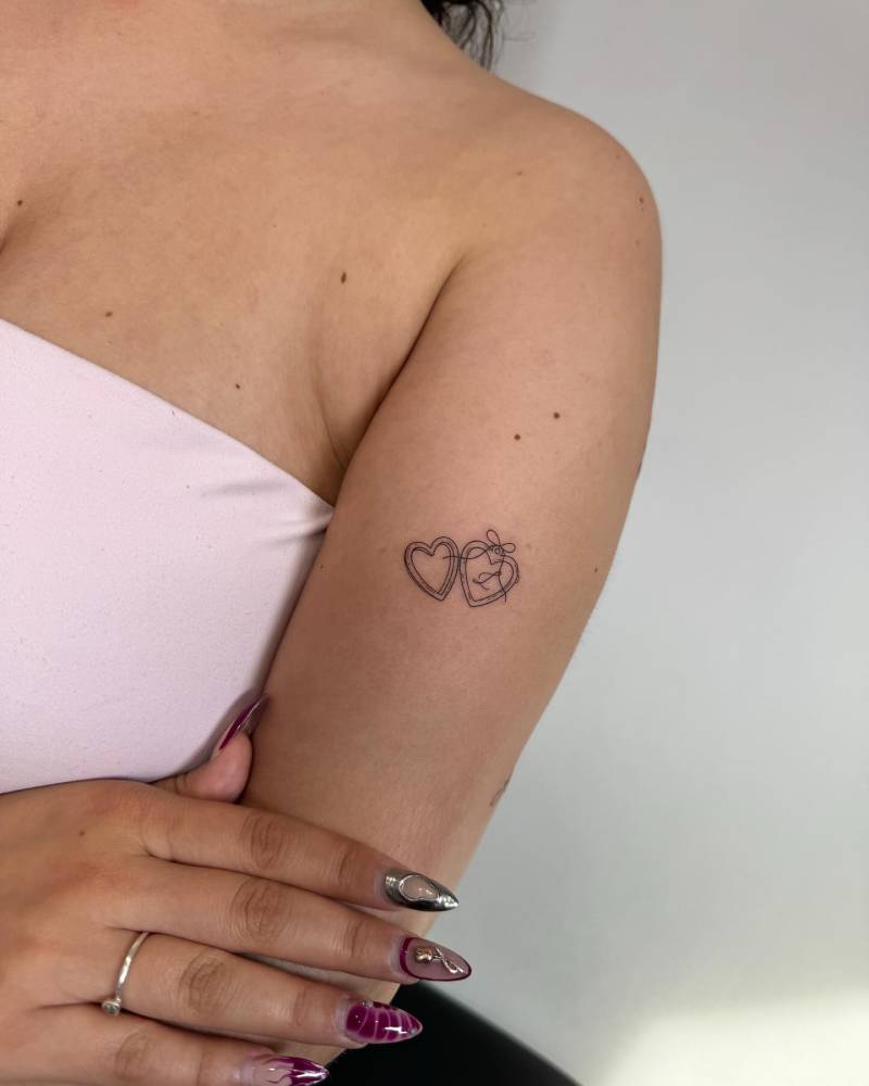 Heart pendant tattoo in fine line style located on the upper arm.